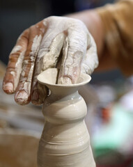 potter while shaping a clay pot on the turning lathe using light pressure on the material with the...