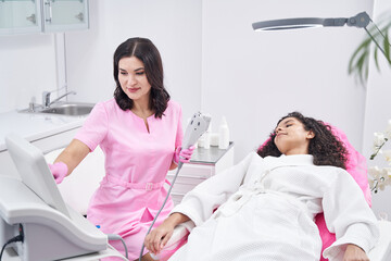 Obraz premium Cosmetologist works with medical apparatus next to woman in chair