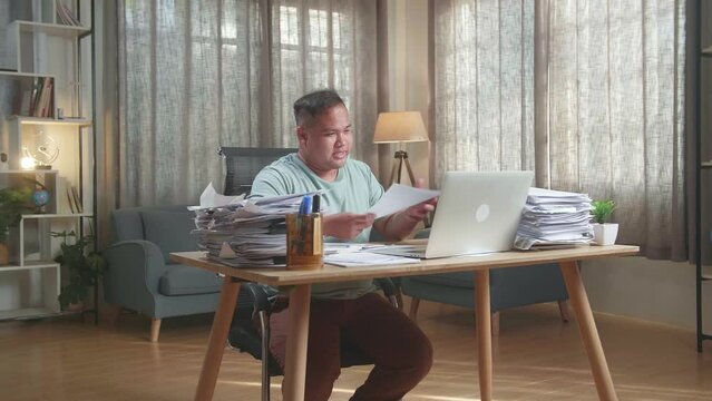 Fat Asian Man With Documents Explaining Work On Paper While Having Video Call On Laptop At The Office
