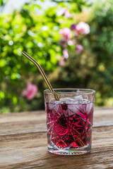 Beautiful ornamental glass with delicious red fruit juice or cocktail with golden metal straw on a wooden garden table