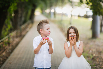 Cute romantic couple of kids with donuts. Brother and sister twins eat pink and chocolate donuts in...
