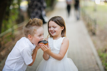 Funny children eat donuts together outdoor, girl child treats boy with donuts