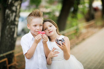 Funny children eat donuts together outdoor, girl child treats boy with donuts