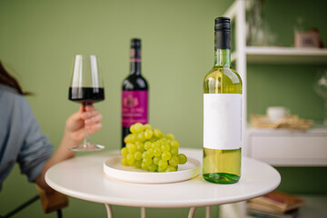 Woman holding glass of red wine over the table with bottles and grapes