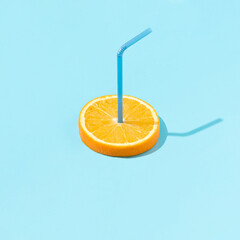 Fresh round orange fruit slice with straw against bright blue background. Minimal juicy citrus food concept. Creative summer vacation idea.