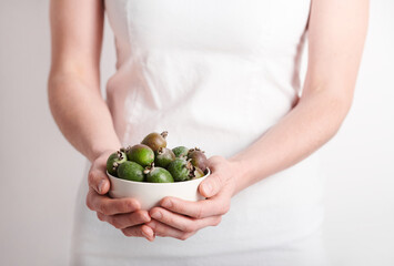 Horizontal medium section shot of unrecognizable woman wearing white clothes holding bowl full of pineapple guava fruits, copy space