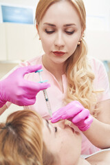 Young beautician with syringe during the procedure of hyaluronic acid in salon