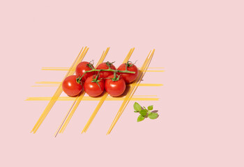 Spaghetti, cherry tomatoes and basil herb, creative arrangement against pastel pink background. Easy tomato sauce and pasta recipe. Traditional Italian kitchen.