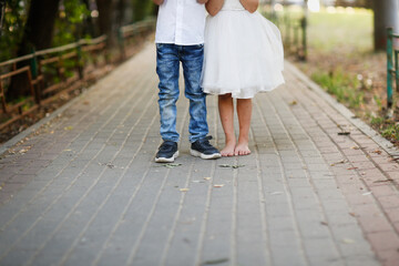 Boy in sneakers and jeans, girl child in white dress and barefoot on the sidewalk in summer