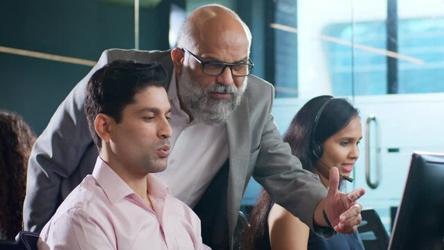 Modern Indian Asian attractive smiling customer support care male or man employee busy working together on computer while interacting or talking to senior boss. Business, Finance, cooperation concept