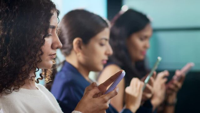 Young modern attractive Indian Asian females, girls, or women in a row are engaged or busy scrolling or browsing on the internet on mobile phones or smartphones. Technology and social media concept