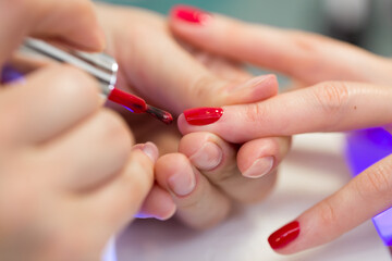 Obraz na płótnie Canvas Manicurist master makes red manicure on young woman hand. Woman nail master doing nails to a girl client at a beauty salon. Care for hands