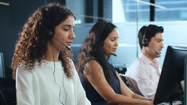 Young modern smiling Indian Asian male and female or mixed gender busy call center employees wearing headsets or headphones interacting with clients in corporate office. Customer care support concept