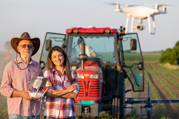 Farmers driving drone in corn field while tractor working in background