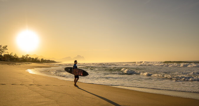Lindo amanhecer na praia do Recreio, com surfista na areia andando para o mar.
