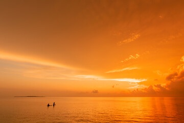 People riding a stand up paddle  on a calm warm sea at an amazing sunrise