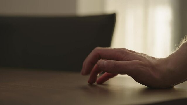 Man hand finger tapping on a walnut table with sunlight from a window behind