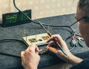Close - up of male hand with wires and retro soldering iron. Soldering process at home