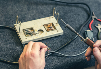 Close - up of male hand with wires and retro soldering iron. Soldering process at home