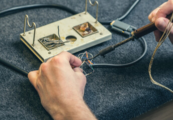 Close - up of male hand with wires and retro soldering iron. Soldering process at home