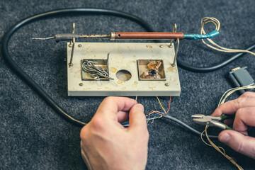 Close - up of male hand with wires and retro soldering iron. Soldering process at home