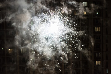 Colorful closeup fireworks light up on the windows of a residential building background.