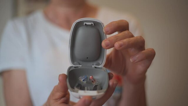 unrecognizable Lady showing modern hearing aids inside a white plastic case held with both hands