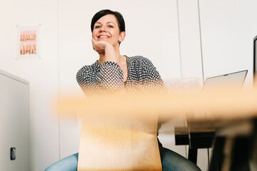 Smiling woman sitting in front of her desk leaning on desk chair and looking at camera
