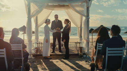 Beautiful Female Queer Couple Exchange Rings and Kiss at Outdoors Wedding Ceremony Near a Sea. Two...