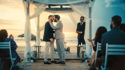 Handsome Gay Couple Exchange Rings and Kiss at a Beach Wedding Ceremony Venue at Sunset. Two Happy...