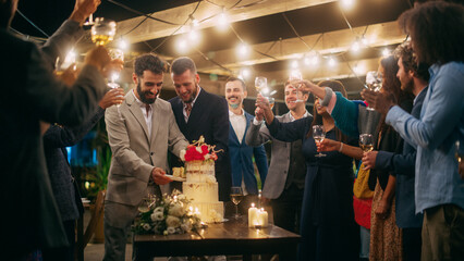 Handsome Happy Gay Couple Celebrate Wedding at an Evening Reception Party with Diverse Multiethnic Friends. Queer Married Couple Standing at a Dinner Table, Kiss and Cut Wedding Cake.