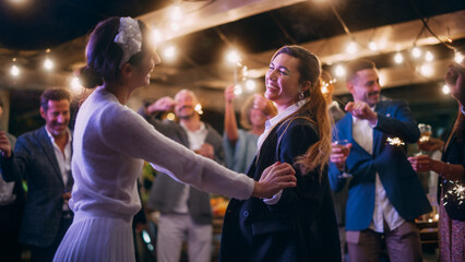 Obraz na płótnie Canvas Beautiful Happy Lesbian Couple Celebrate Wedding at an Evening Reception Party with Diverse Multiethnic Friends. Queer Newlyweds Dancing and Kissing at a Restaurant Venue. LGBTQ Relationship Goals.