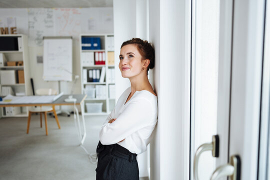 young businesswoman leans against a pillar in the office and looks up thoughtfully