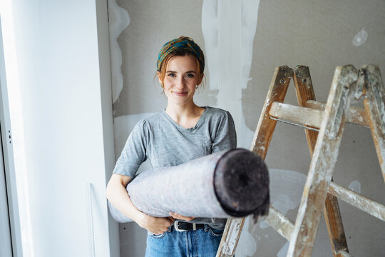Young woman renovating her bedroom and has a painter carpet in her hand
