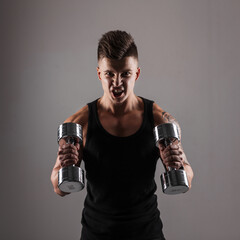 Fototapeta na wymiar Cool athletic bodybuilder man with a muscular body is training hard with metal dumbbells in the studio against a dark background