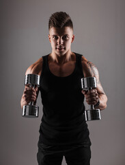 Fototapeta na wymiar Handsome sports strong guy model with hair in a black T-shirt working out with dumbbells on a dark background in the studio. Sports and healthy lifestyle