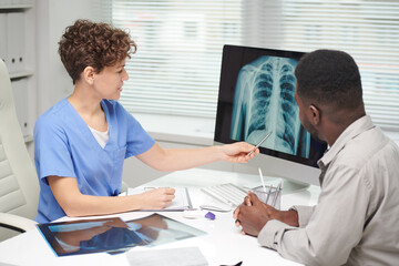 Modern professional medical specialist demonstrating x-ray shot to African American patient on...