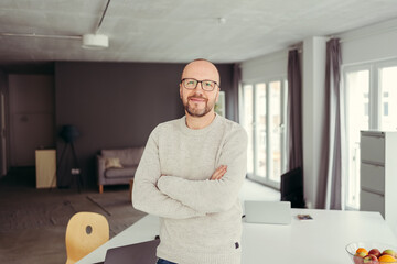 Man with glasses stands in office and looks into camera with folded arms