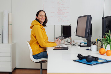 Woman in yellow sweater sits at desk and looks at camera laughing