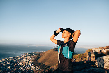 Woman hiker adjusting cap with closed eyes. Female trail runner feeling taking rest during a hike.