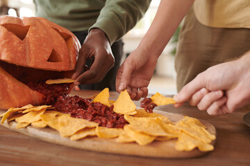 Close-up of unrecognizable interracial friends eating nachos with sauce at Halloween party
