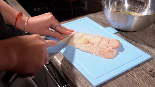 homemade fried fish in batter step by step. step 2 cutting the fillet of raw white fish on the board with a large knife into pieces