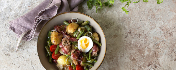 a bowl of liege salad with potatoes, green beans and bacon on a light table