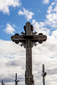 Vertical photo of big cross - brown wooden handmade carpentry art at cross of hills near Šiauliai, Lithuania. Great ornamental timber cross against cloudy sky