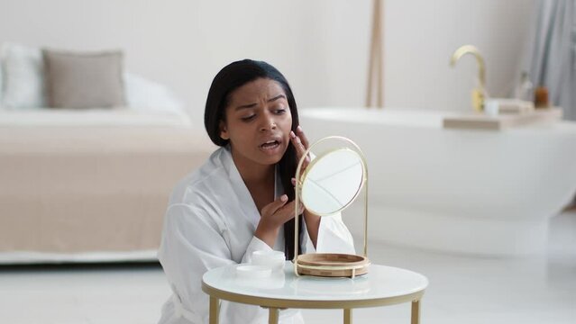Acne problem. Young unhappy african american woman looking at her problematic skin, examining pimples