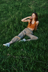 A woman lies on fresh spring green grass in a park without mosquitoes or ticks and enjoys relaxing while watching the sunset. The concept of safe outdoor recreation