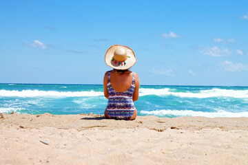 Young woman on the sand looking into waving sea.