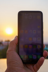 a hand holding a smartphone taking a photograph at sunset