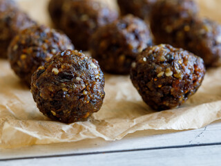 Healthy organic homemade delicious energy balls: chocolate balls cakes made from raisin, prune, dates, walnut, figs on baking paper against white background. Close up macro