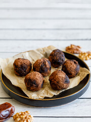 Healthy homemade delicious energy balls: chocolate ball cakes made from raisin, prune, dates, walnut, figs in black plate against white background, covered with cocoa carob powder. Close up copy space